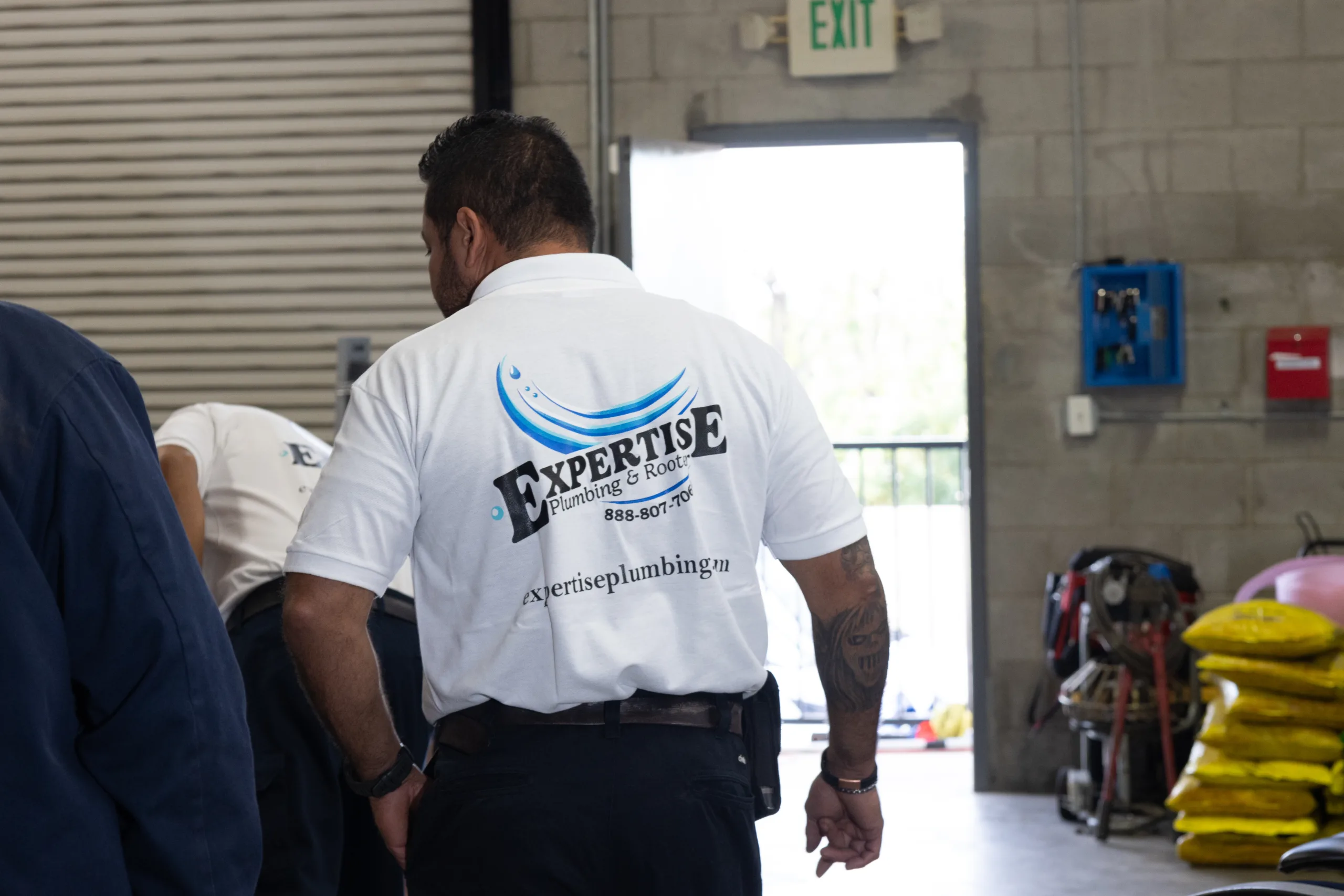 Expertise Plumbing technicians getting ready for a job. In center is back of tech showing Expertise logo on shirt.