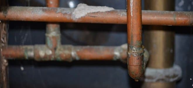 A close-up of a pinhole leak on a corroded copper pipe